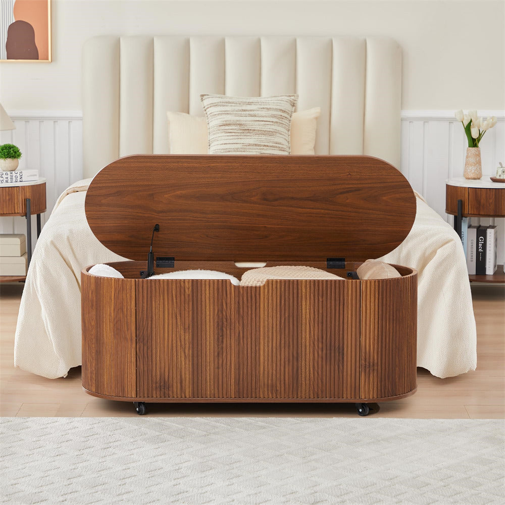 Wooden storage bench in a bedroom setting with a bed and headboard in the background.