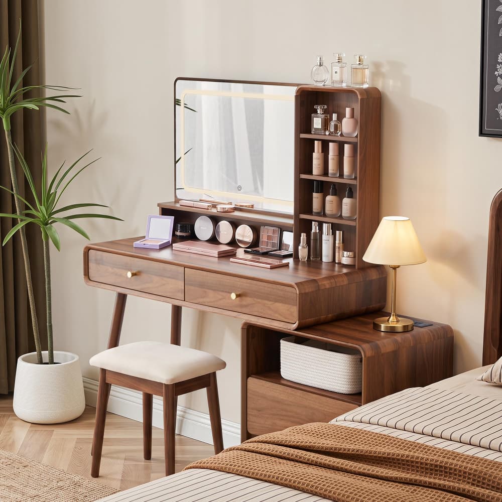 A wooden vanity desk with an attached mirror, open shelving, and a matching stool in a styled bedroom setting next to a bed.