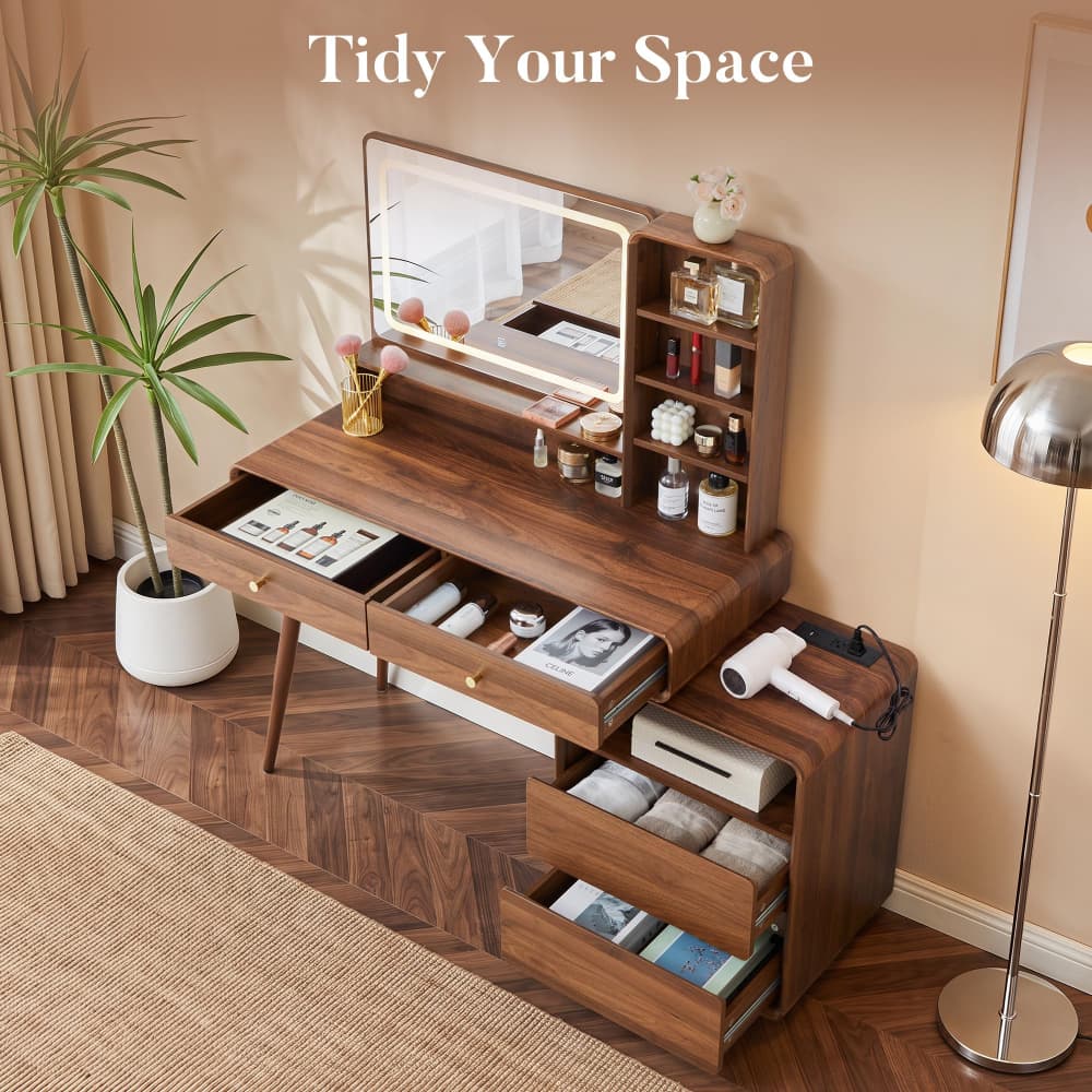 A dark walnut wood vanity desk with an integrated mirror, open drawers, and storage shelves, styled in a warm beige room with a potted plant and floor lamp.