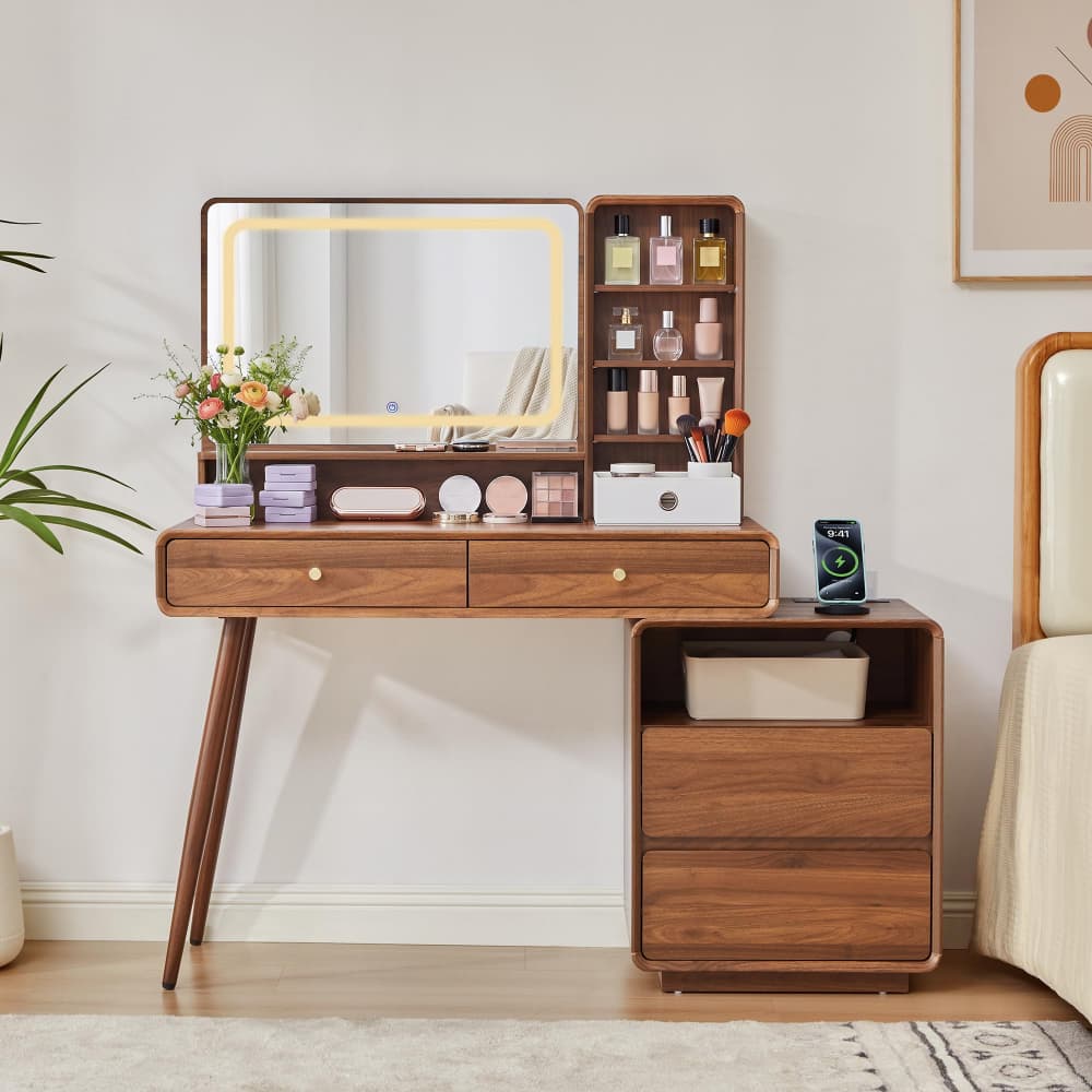 A mid-century modern wooden makeup vanity table with an illuminated rectangular mirror, open shelving, drawers, and a matching side cabinet, styled in a bedroom setting.