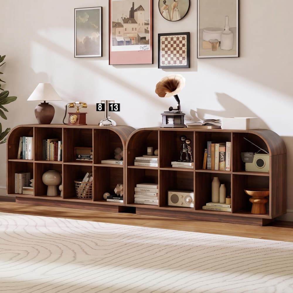 A long, low wooden bookcase with multiple arched cubby shelves, styled with books, a lamp, a vintage gramophone, and decor in a bright room with framed wall art and a rug.