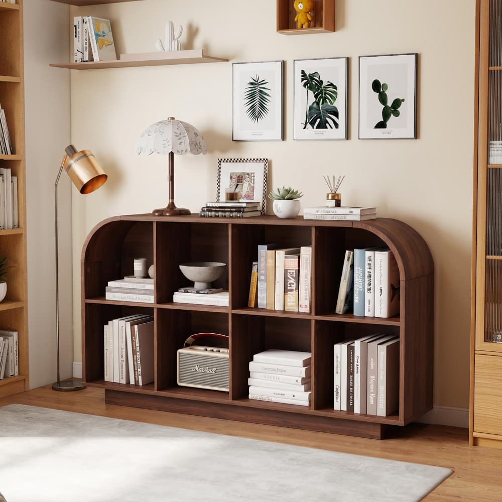 A dark brown wooden bookcase with arched top details, styled with books, a lamp, and small decor items in a warm, modern room setting.