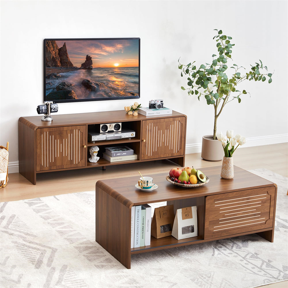 Wooden TV stand with a television displaying a sunset over water, a coffee table with books and fruit, and a plant in the corner.
