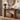 A medium brown wooden console table styled in a warm, rustic entryway. The table features a thick rectangular top and legs with an open lower shelf holding a wicker basket of books.