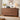 A mid-century modern wooden dresser with nine drawers in a warm walnut finish, styled in a cozy living room setting with a lamp, radio, and flowers on top.