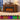 A brown wood-look electric fireplace with glowing orange and yellow faux flames, shown in a styled room setting with a lamp, books, and decorative items on the mantel. Text below reads 'Set the Mood with Colorful Flames' and shows eight flame color options.