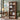 A tall wooden bookcase with a warm medium-brown finish stands in a styled home office. The bookcase features an arched top shelf, four open middle shelves, and two lower storage bins.