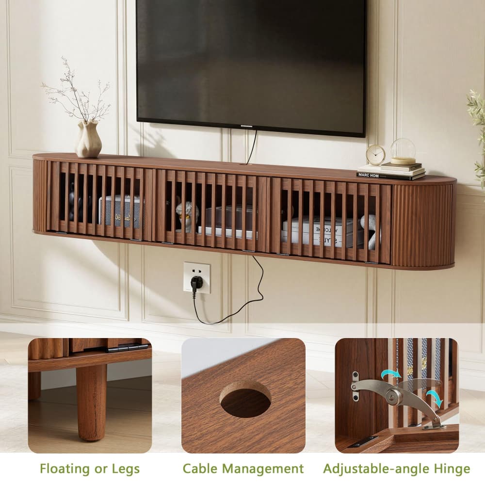 A floating wooden TV stand with a warm brown finish, mounted on a cream paneled wall below a black television. The stand features vertical slats on the front, open storage compartments, and a cable management hole.