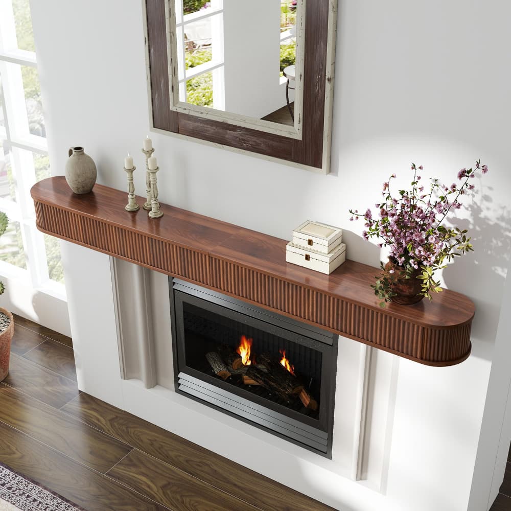 A floating wooden mantel shelf mounted above a built-in electric fireplace, styled with decorative vases, candle holders, a stack of books, and a potted purple flower arrangement in a bright living room.