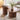 Two modern round nesting coffee tables with fluted pedestal bases in a warm medium brown wood finish, styled in a bright living room with a beige armchair, a white vase with greenery, and a stack of books on the smaller table.