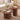 Two round wooden coffee tables with fluted pedestal bases in a styled living room. The larger table holds a vase of white flowers, a cup and saucer, and an open magazine, while the smaller matching table beside it holds two stacked books.