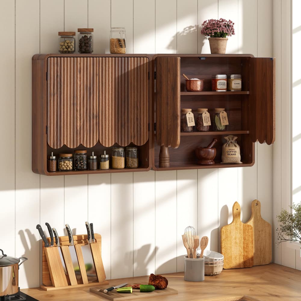 A dark brown wooden kitchen wall cabinet with scalloped doors, shown open to reveal shelves with jars, a mortar and pestle, and a small pot. The cabinet is mounted on a white paneled wall above a wooden countertop with knives, cutting boards, and kitchen utensils.