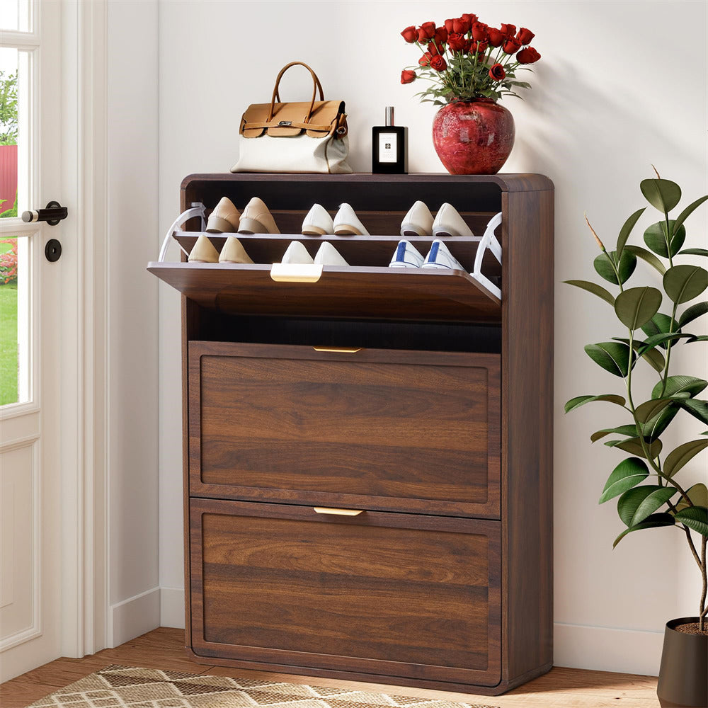 Wooden shoe cabinet with open door displaying shoes, next to a plant and a vase with flowers.