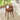 A round wooden side table with three legs and a slatted drawer front, styled in a bright living room next to a sofa with a vase of flowers and a cup of coffee on top.