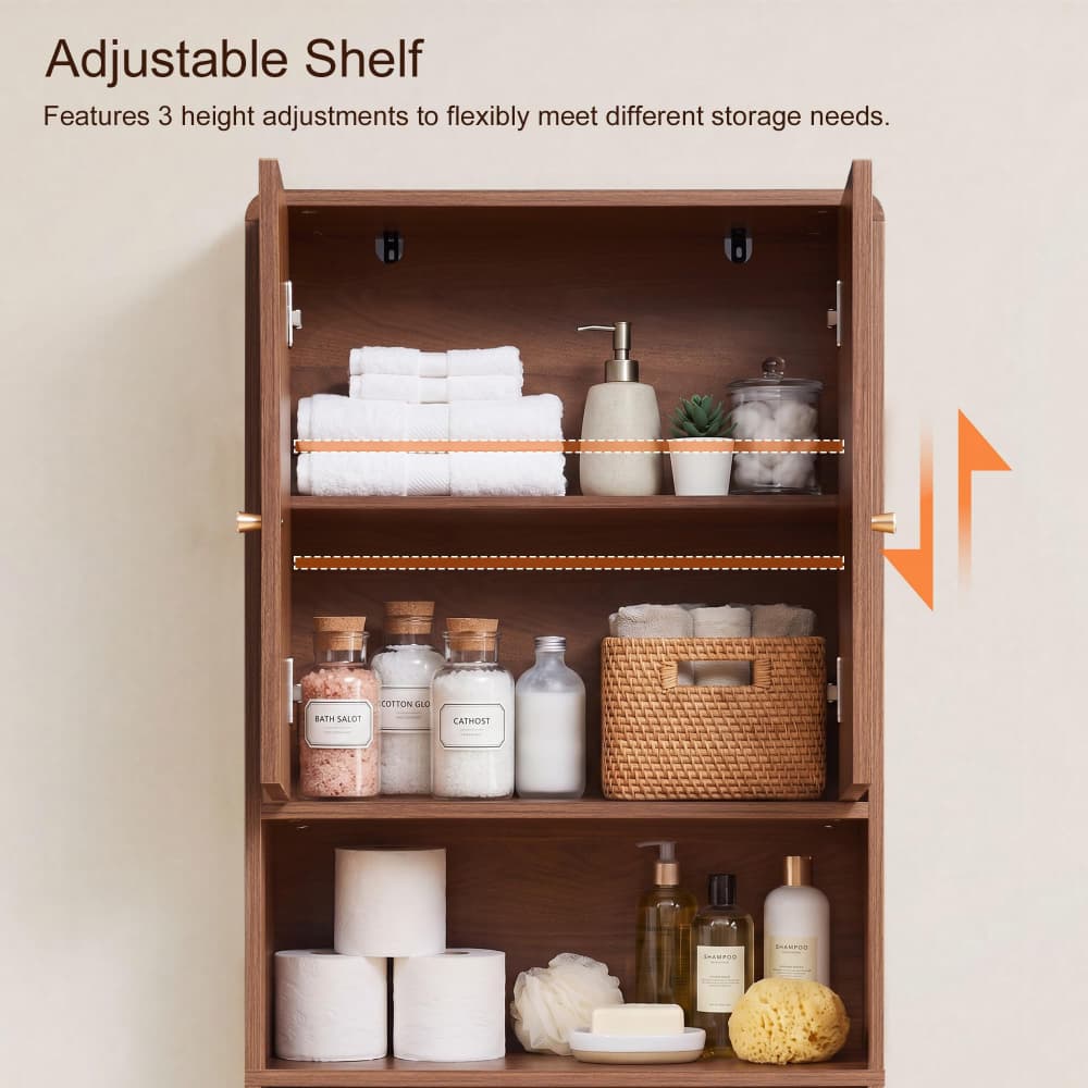A wall-mounted wooden bathroom cabinet with three adjustable shelves, shown open and styled with towels, bottles, a basket, and bath accessories. Text at the top reads 'Adjustable Shelf' with a note about three height adjustments, and orange arrow graphics indicate adjustability.