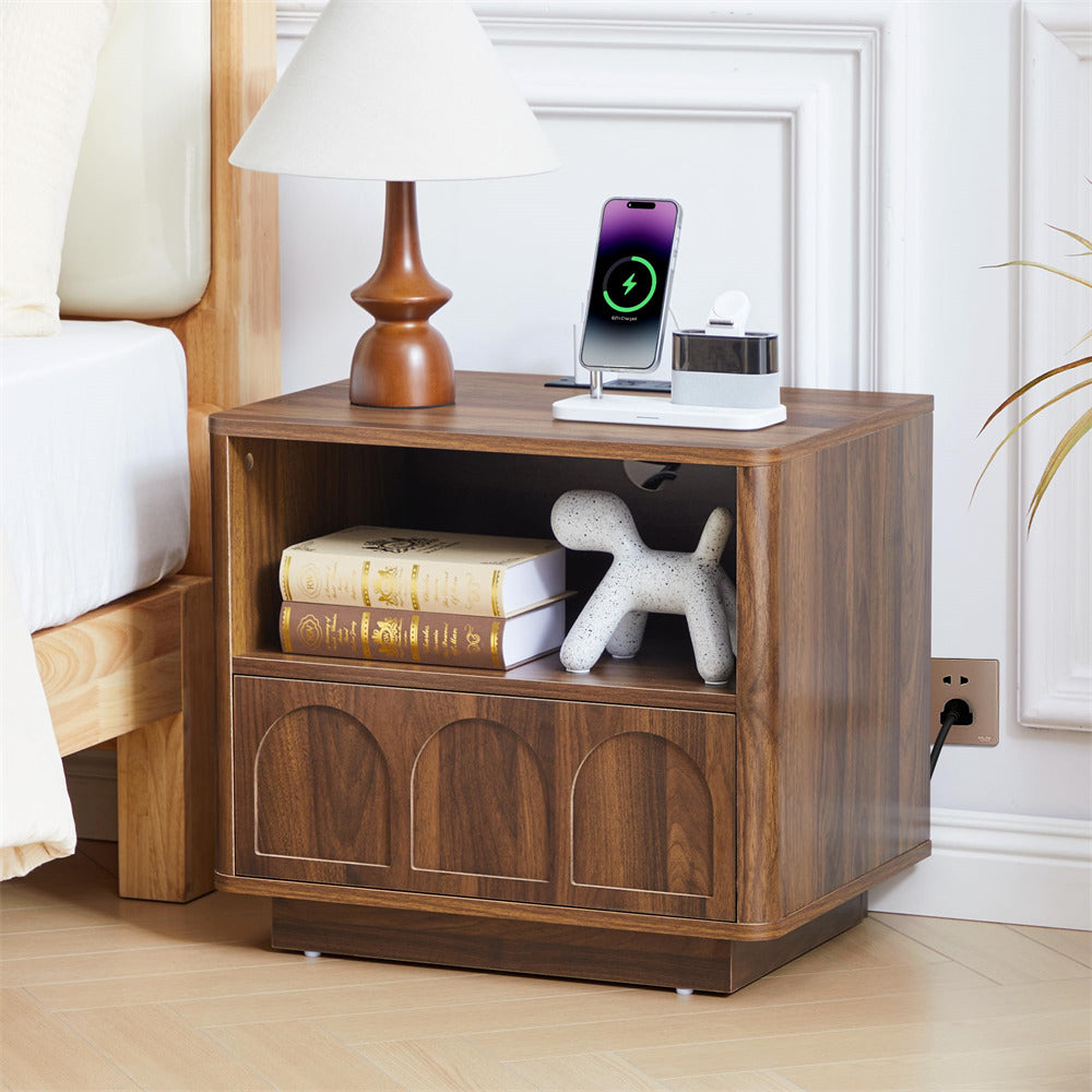 Wooden nightstand with books, lamp, and electronic devices in a bedroom setting