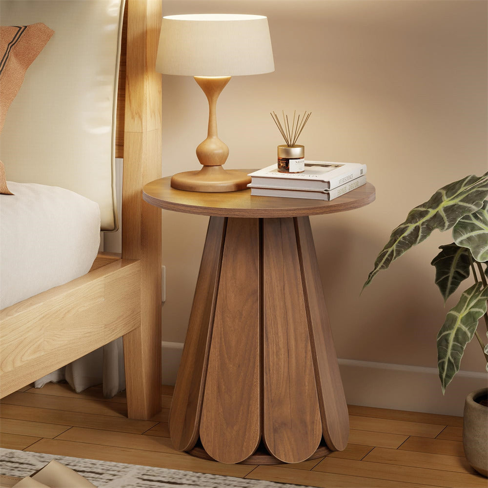 Wooden side table with lamp and books next to a bed in a bedroom setting