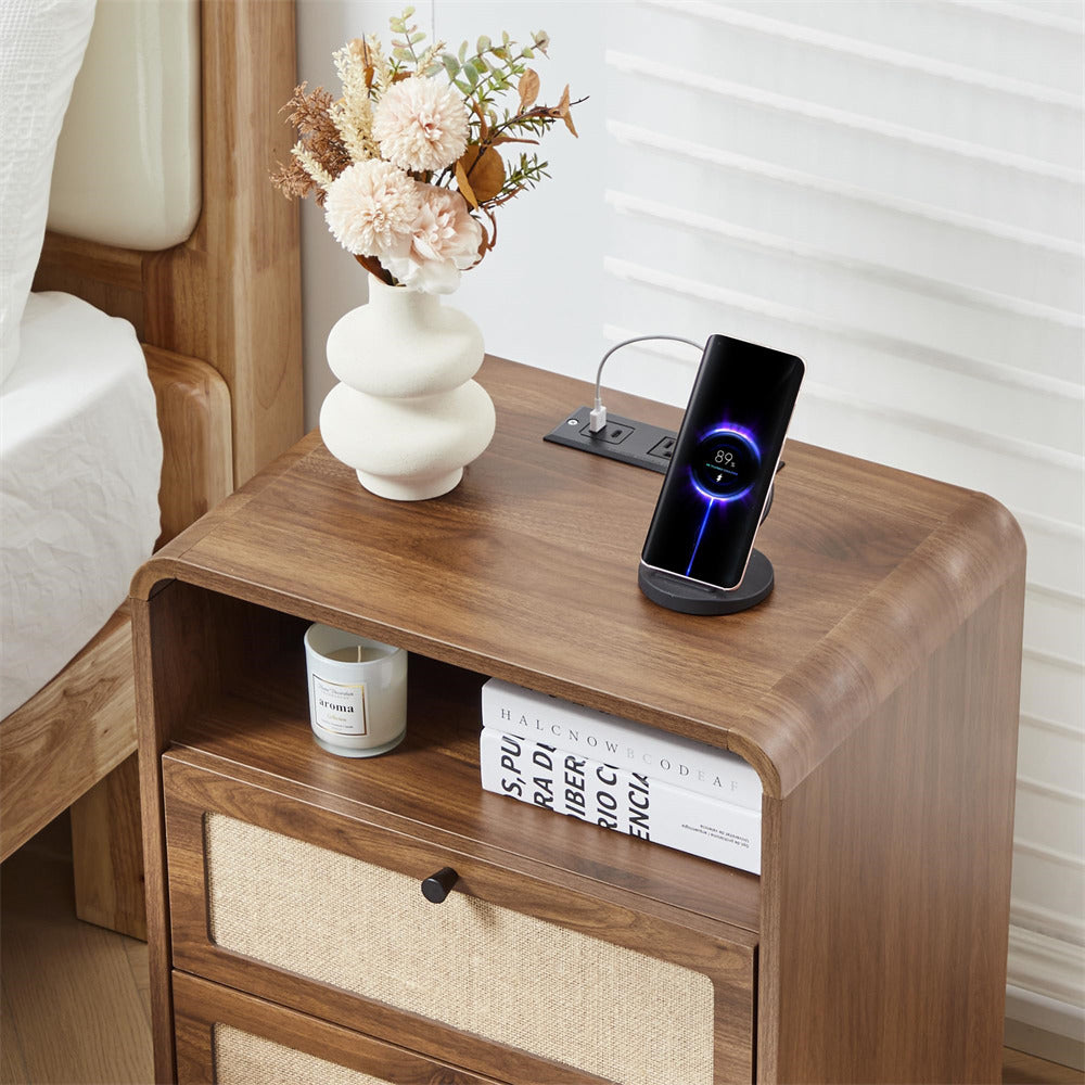 Wooden nightstand with a smartphone on a stand, books, and a vase with flowers.