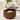 A modern round coffee table in a warm medium brown wood finish, featuring a fluted slatted cylindrical base with a built-in cream cushion and a hinged top surface holding a laptop and vase of flowers, set in a bright living room.