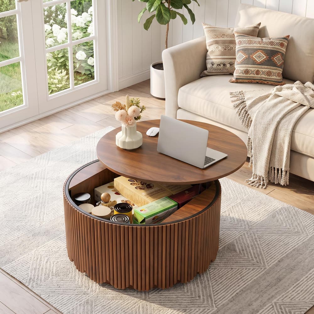 A round wooden coffee table with a fluted lower base and a hinged top section, styled in a bright living room with a laptop, vase, and books on top and open storage visible below.