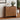 Wooden dresser with decorative items in a room with plants and a framed picture on the wall.