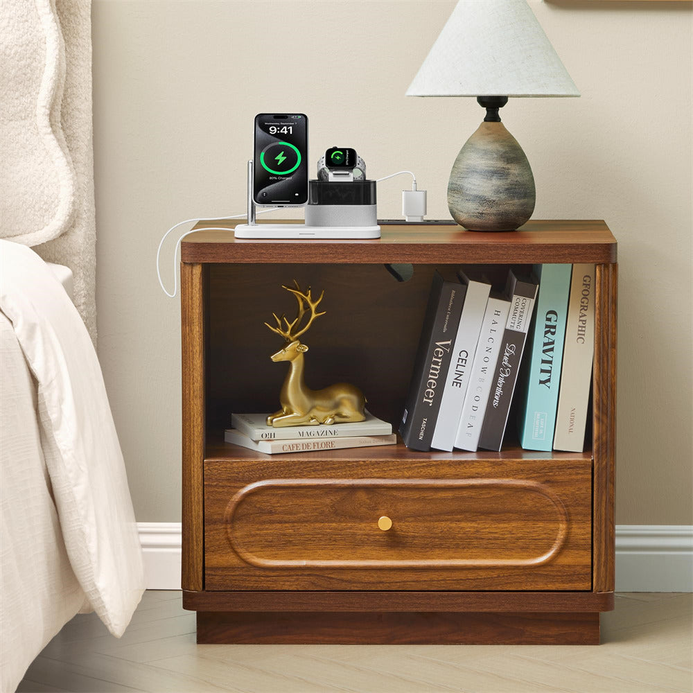 Wooden nightstand with books, a lamp, and electronic devices in a bedroom setting.