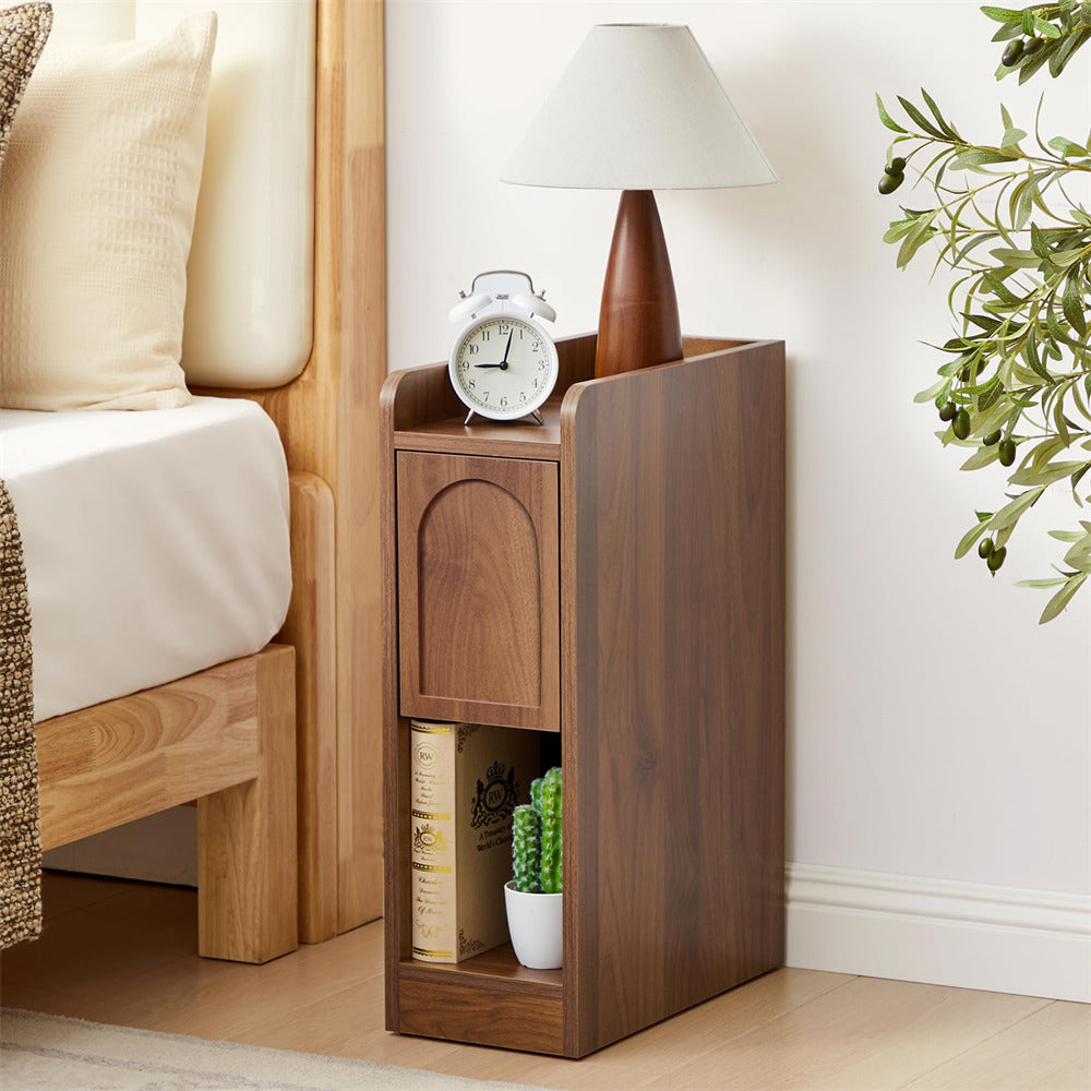 Wooden nightstand with lamp, clock, and books next to a bed in a bedroom setting.