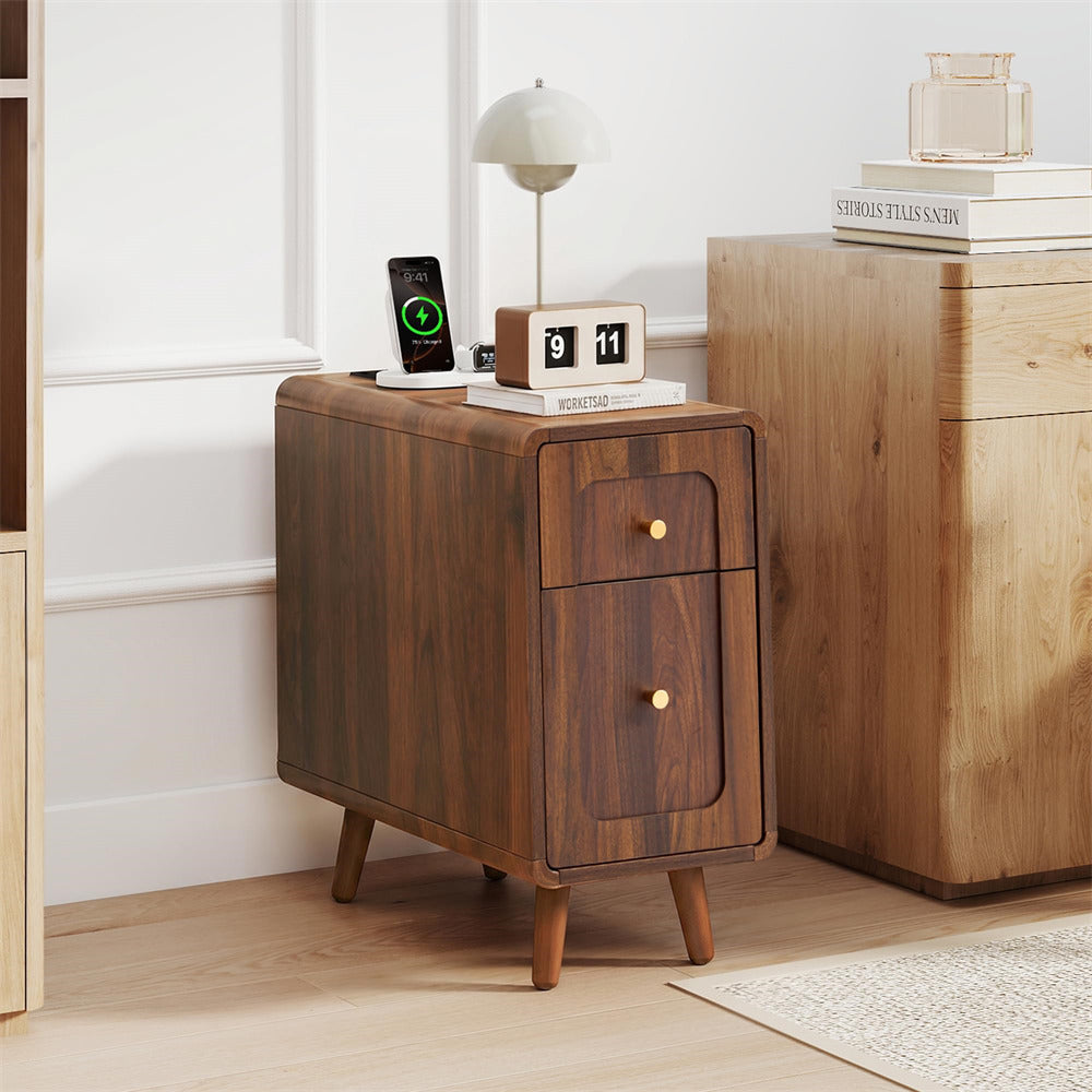 A mid-century modern wooden nightstand with two drawers and gold knobs, styled in a bright room next to a larger wooden cabinet.