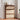 Wooden shoe cabinet with open door revealing shoes, placed in a room with light-colored walls and a window.