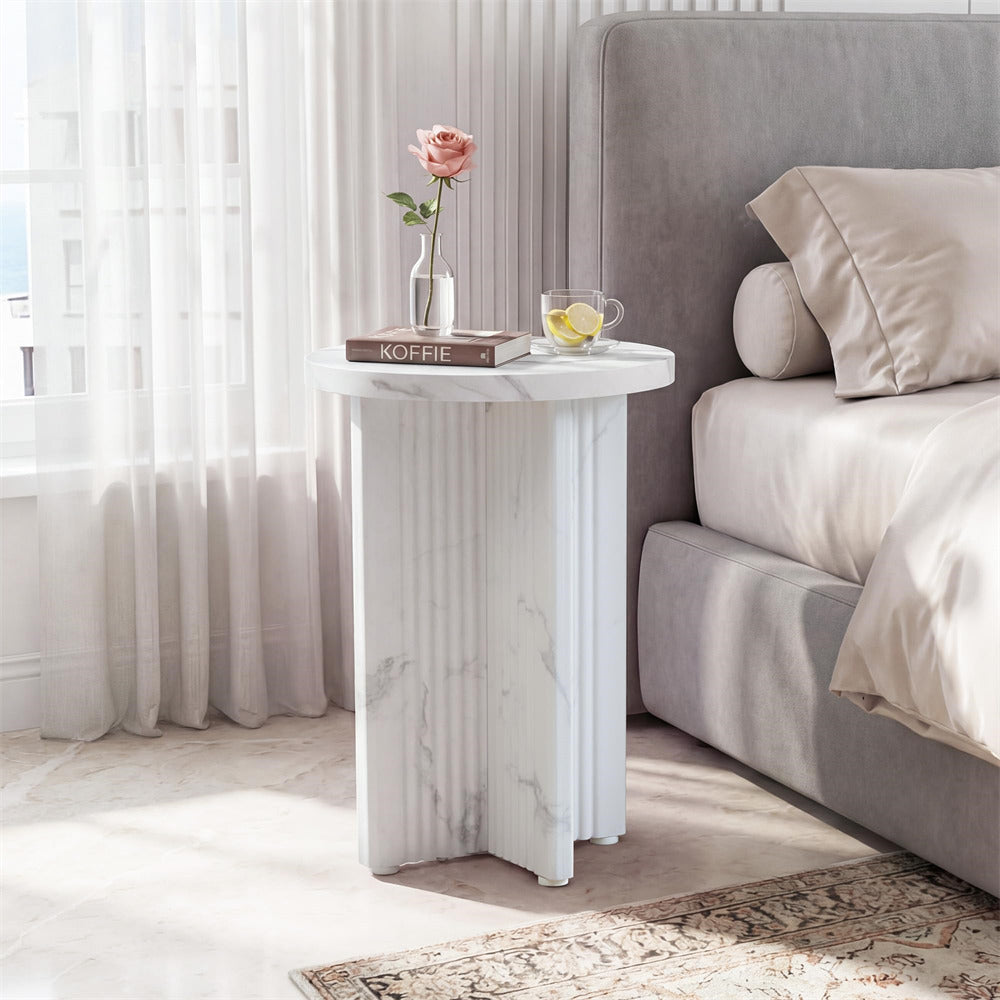 Marble side table with a vase of flowers and a book next to a bed in a bedroom.