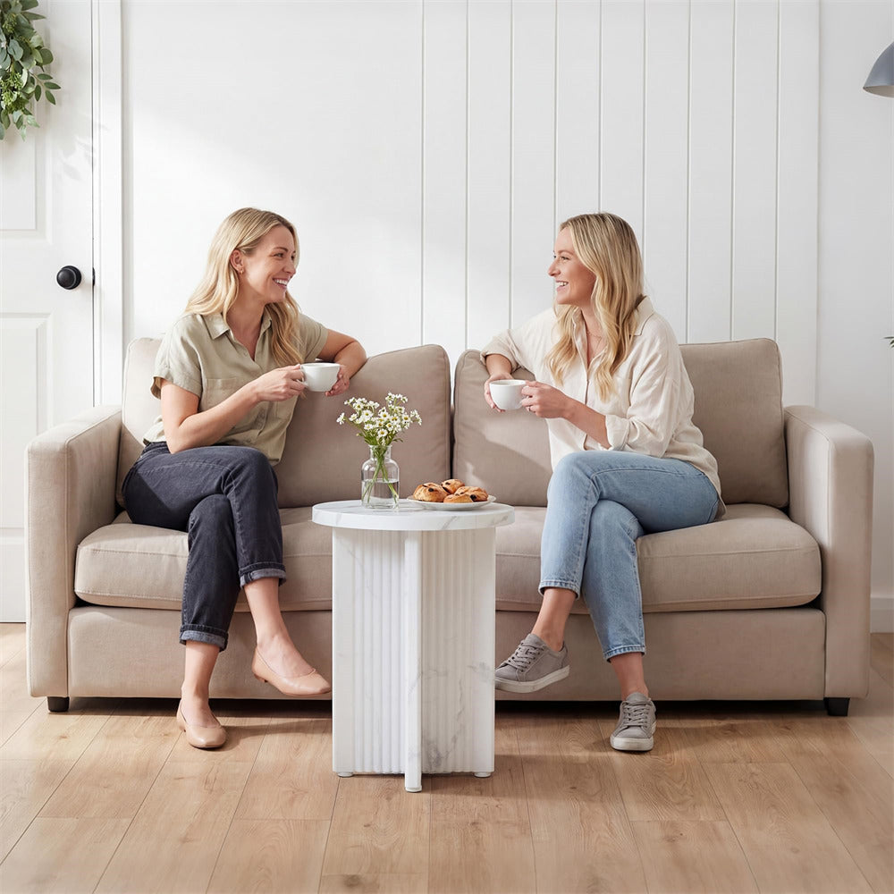 Two women sitting on a couch in a living room, holding cups and smiling.
