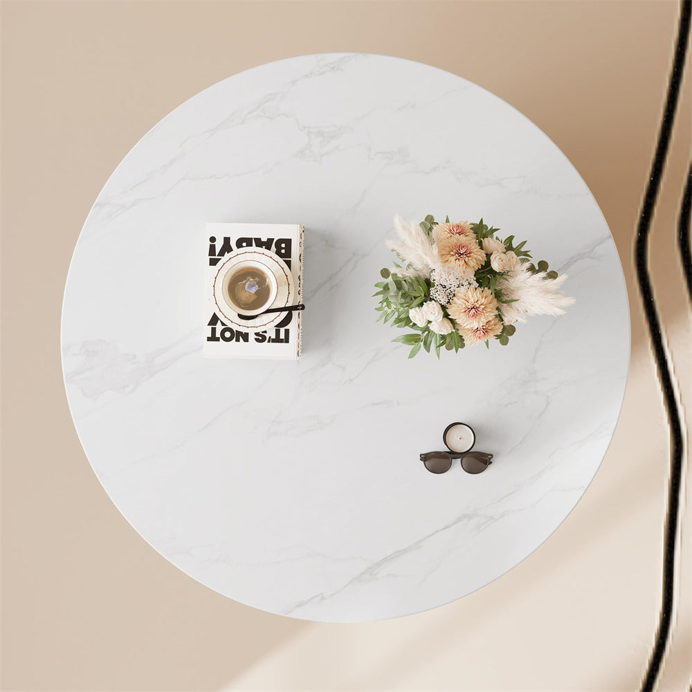 Round marble table with decorative items including a small clock, candle, and floral arrangement on a beige background.