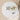Round marble table with decorative items including a small clock, candle, and floral arrangement on a beige background.