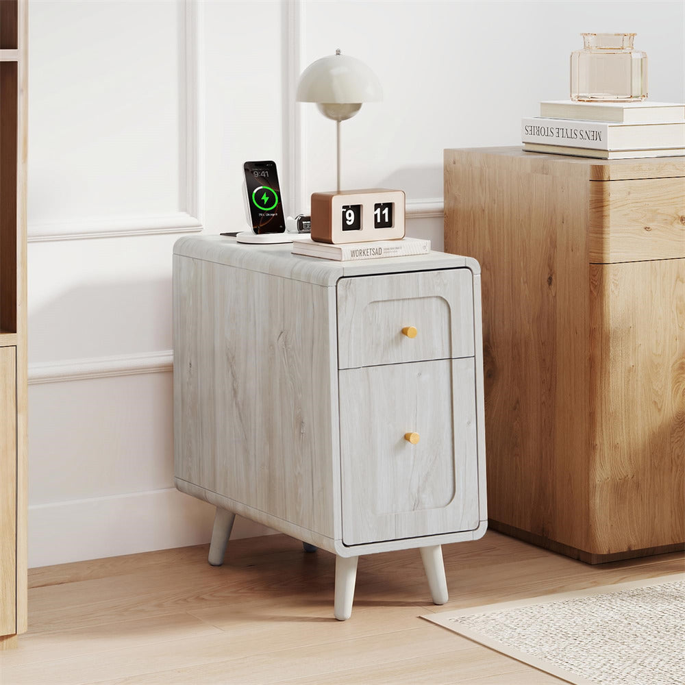 A light gray wood-grain two-drawer nightstand with small tapered legs and round gold knobs, styled in a bright room next to a wooden cabinet.