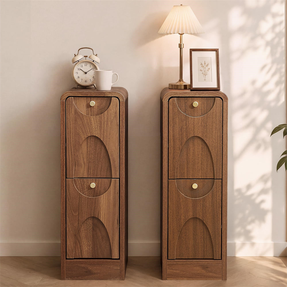 Two matching narrow wooden side tables or cabinet stands with arched drawer fronts and round brass knobs, shown in a styled interior scene with a clock, mug, lamp, framed print, and plant shadows on the wall.